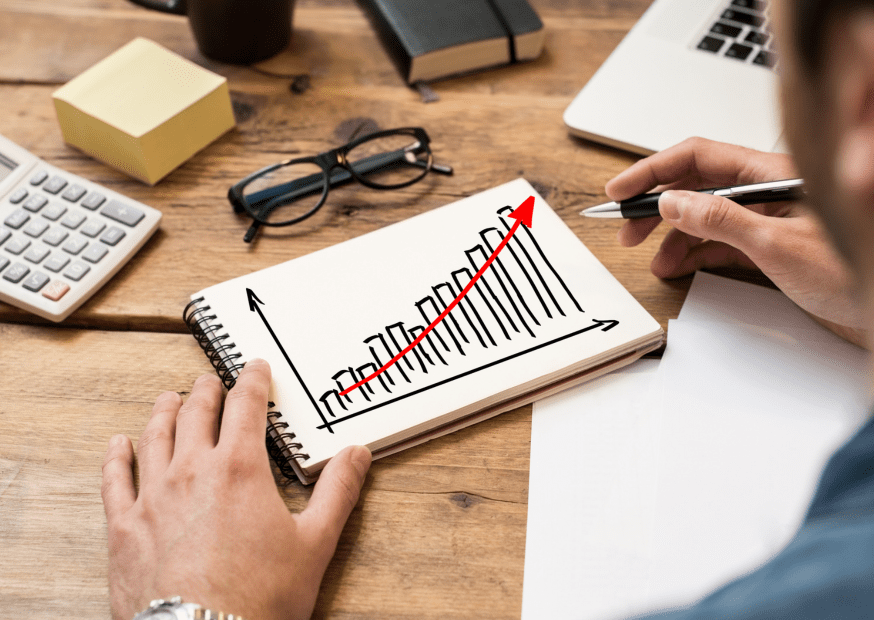 "Explore effective strategies for business growth with this visual, showcasing a hand-drawn bar graph and upward trend line, accompanied by a laptop, calculator, glasses, and sticky notes. Enhance your financial and strategic planning skills to drive positive business growth.