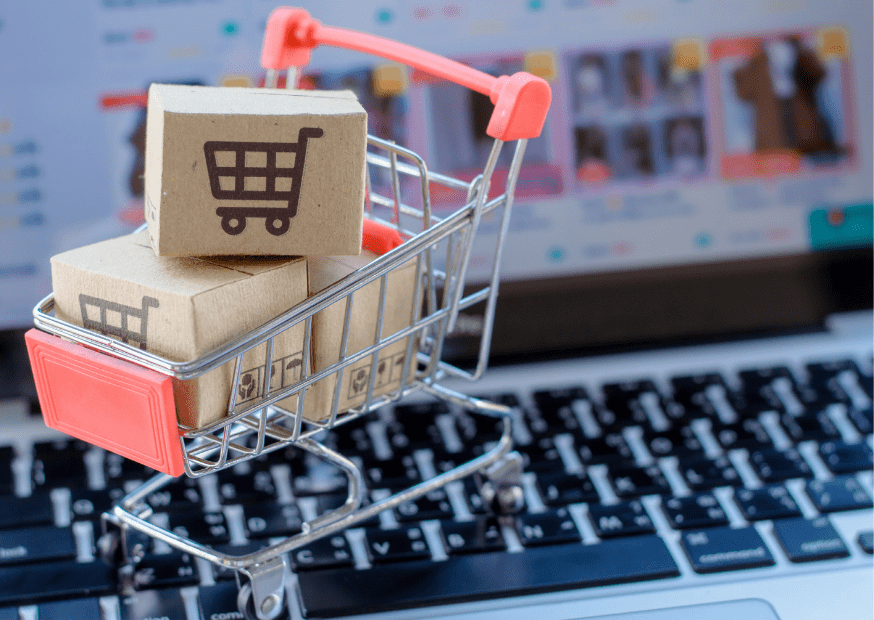 A miniature shopping cart is standing on a laptop keyboard symbolizing e-commerce.