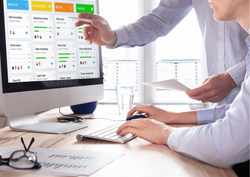 Two professionals in an office environment in front of a computer screen discuss the project of MVP development for a startup