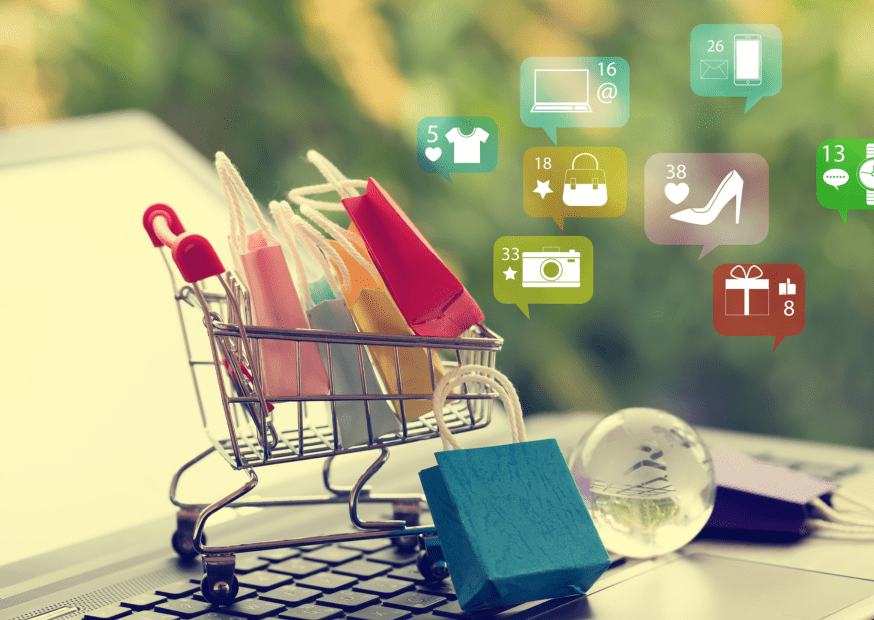 Instant e-commerce concept with a miniature shopping cart filled with colorful shopping bags on a laptop keyboard, surrounded by digital icons representing online shopping features.